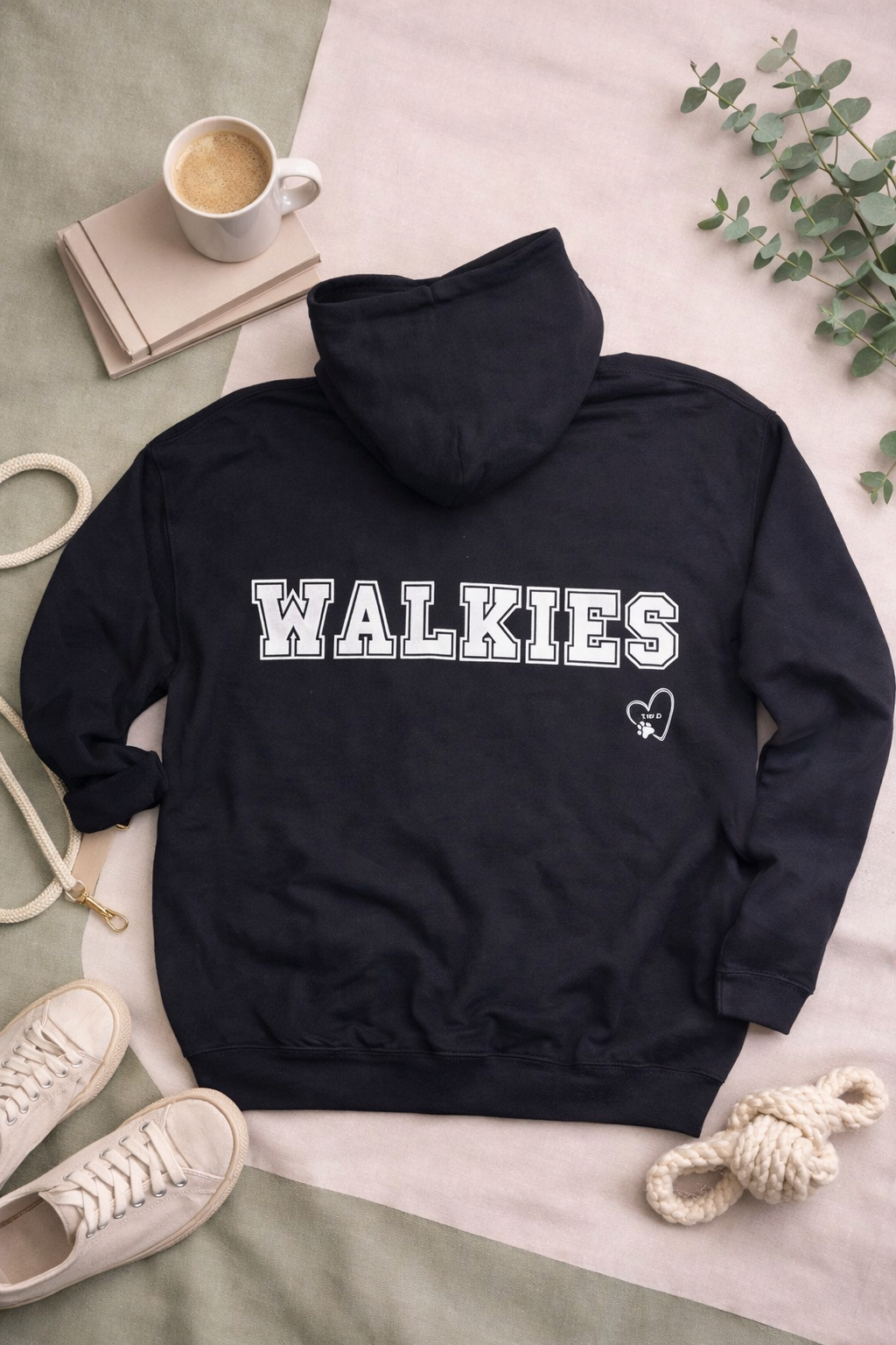 Black hoodie with 'WALKIES' text on a light surface with shoes and a cup in the background