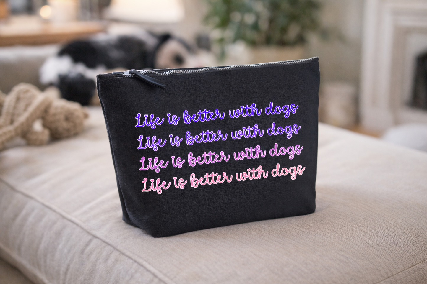 Black pouch with 'Life is better with dogs' text on a couch with a dog in the background