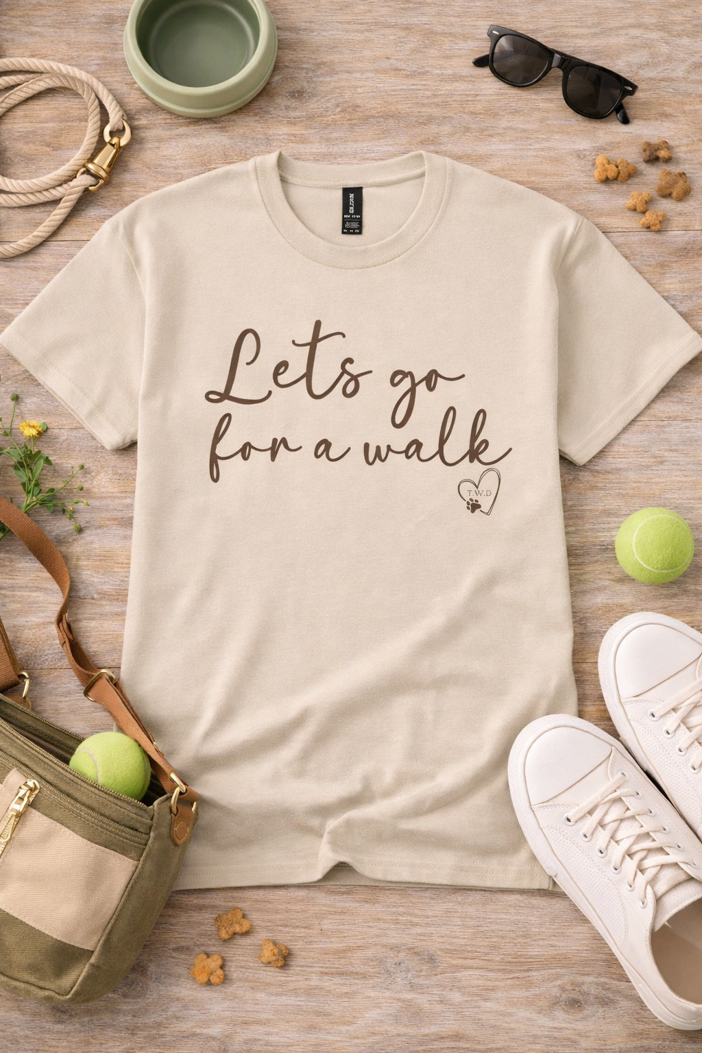 Beige t-shirt with 'Let's go for a walk' text on a wooden surface with accessories.