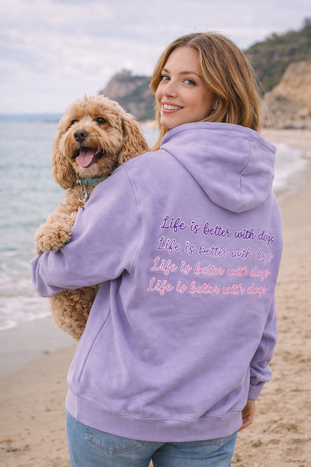 Woman wearing a lavender hoodie with text on the beach holding a dog.