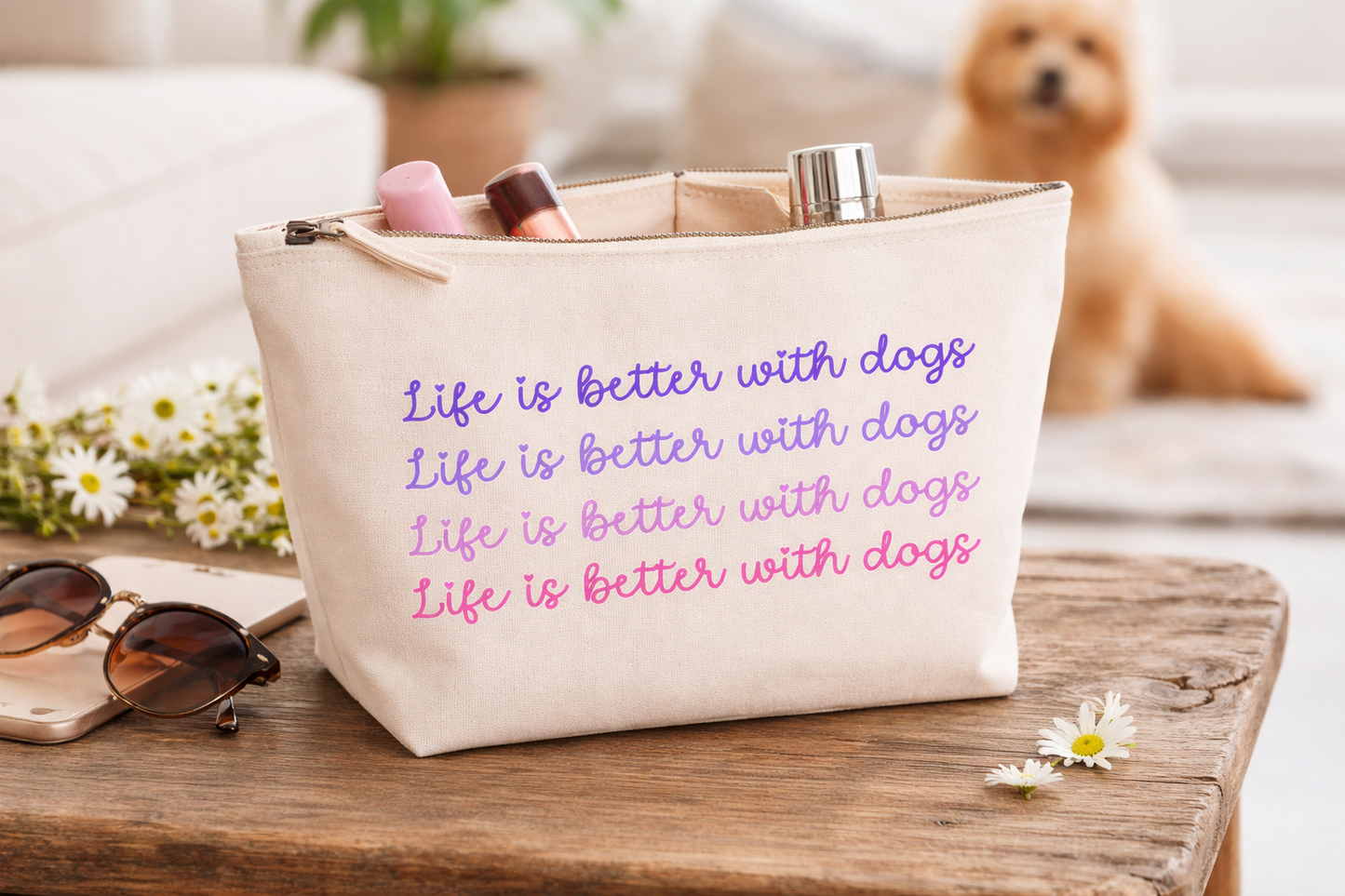 Beige tote bag with 'Life is better with dogs' text, sunglasses, and flowers on a wooden surface.