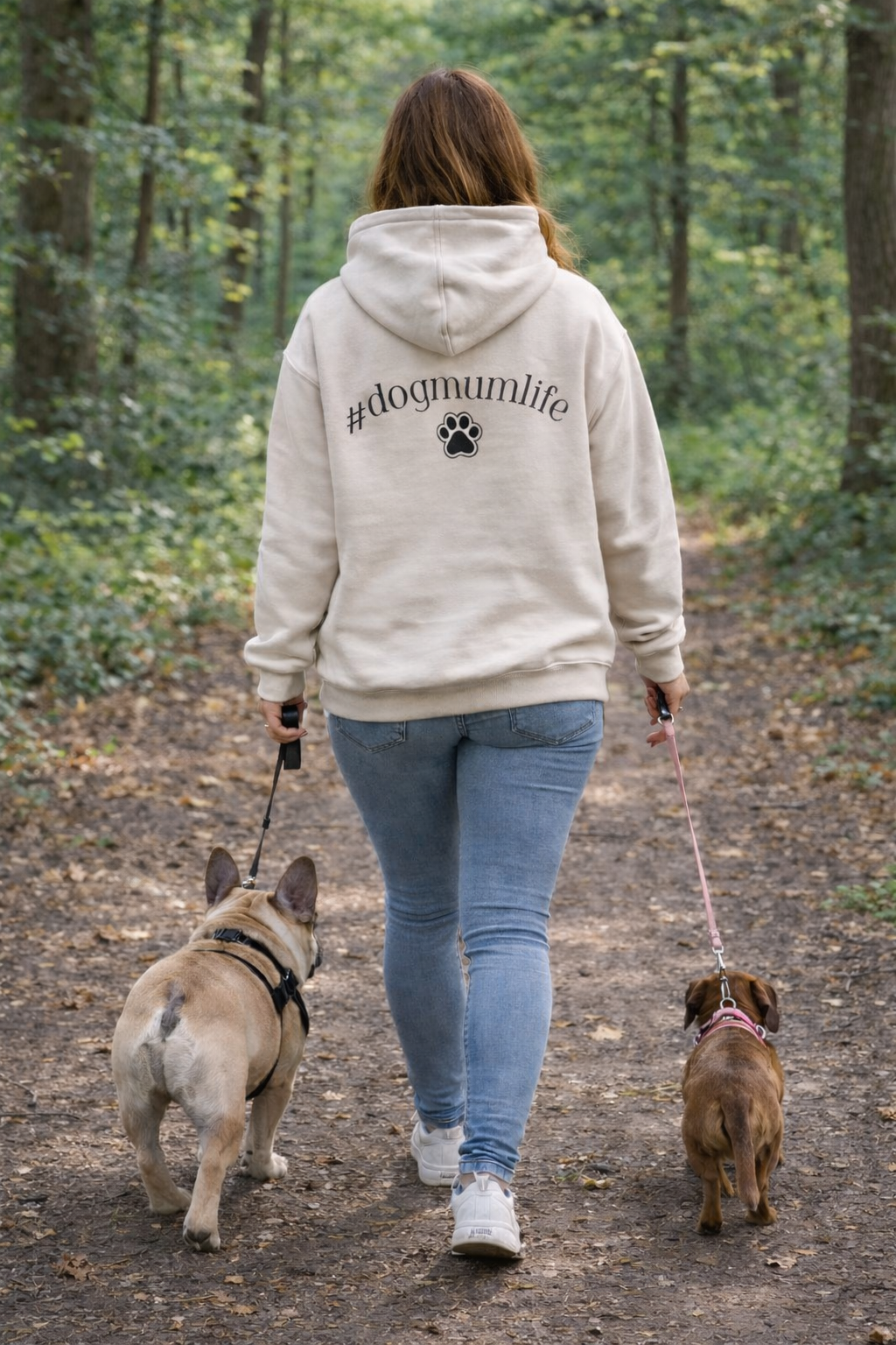 Person walking two dogs on a path in a forest wearing a hoodie with '#dogmumlife' text.