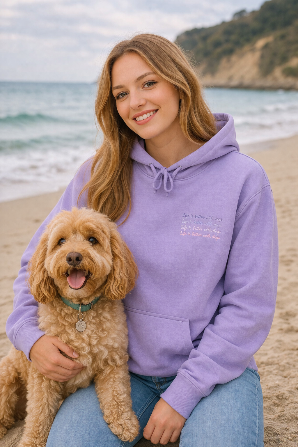 Woman in a purple hoodie sitting on a beach with a dog