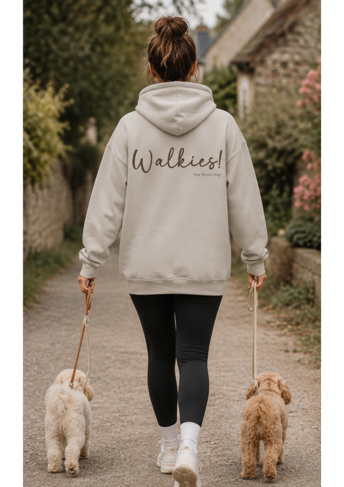 Female dog owner walking two small dogs wearing a sand Walkies hoodie by That Woofin Dog, showcasing the large back print design on a countryside walk.