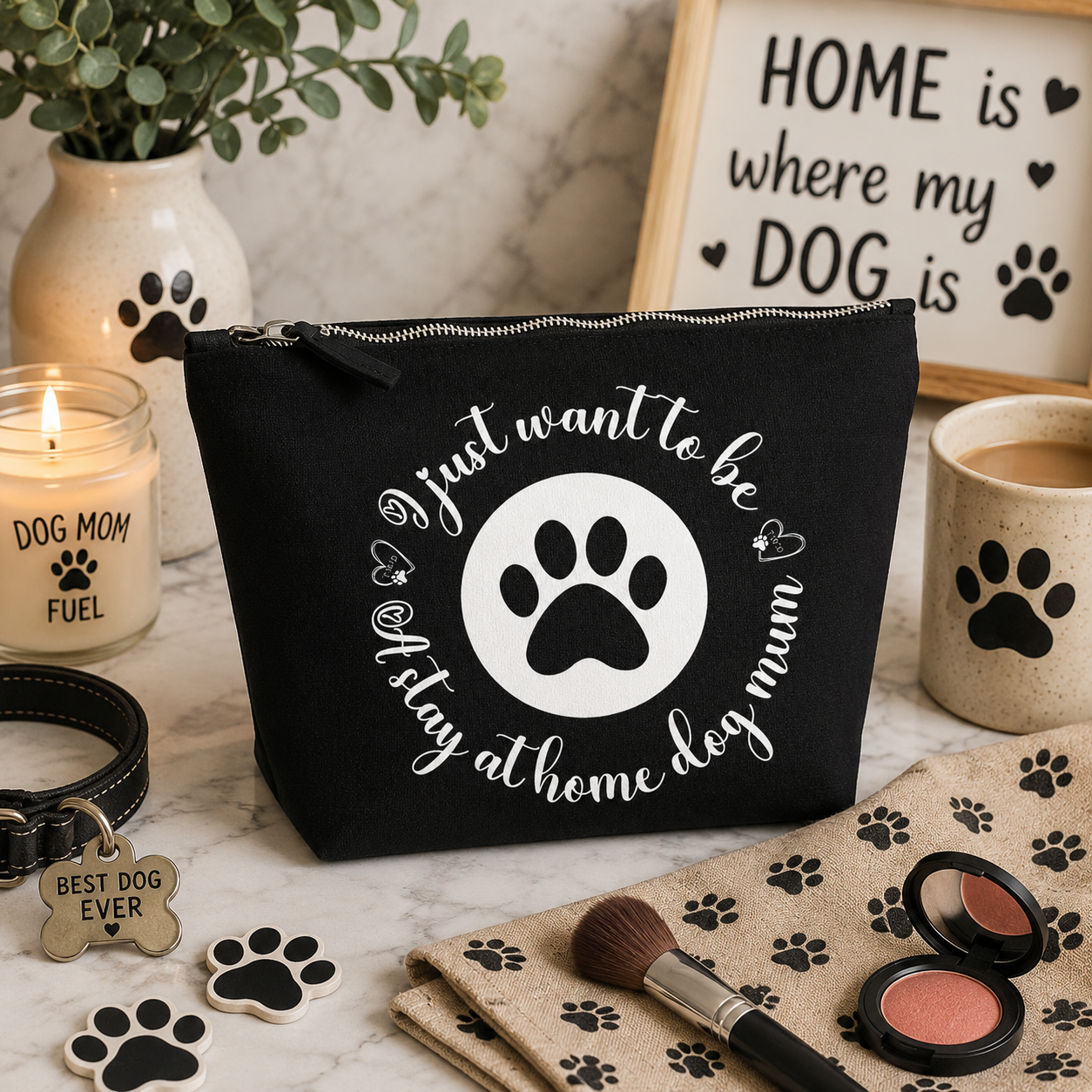 Black canvas makeup bag featuring the "Just Want to Be a Stay at Home Dog Mum" design with a white paw print motif, displayed on a cosy dog-themed home background with paw-print décor, candles, framed dog signs, makeup brushes, blush, and stylish dog lover accessories. Perfect for dog mums and pet lovers.